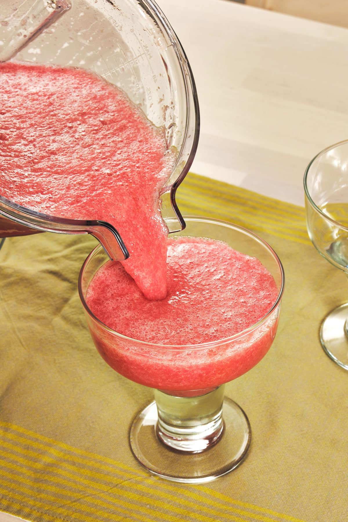 Pouring fresh prickly pear margarita into glass from pitcher.