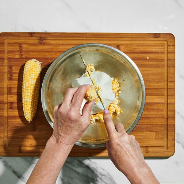 Cutting kernels from sweet corn cob in bowl.