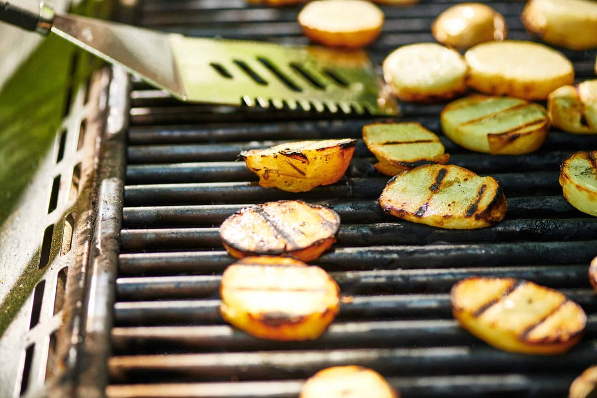 Flipping potato slices on grill with spatula.