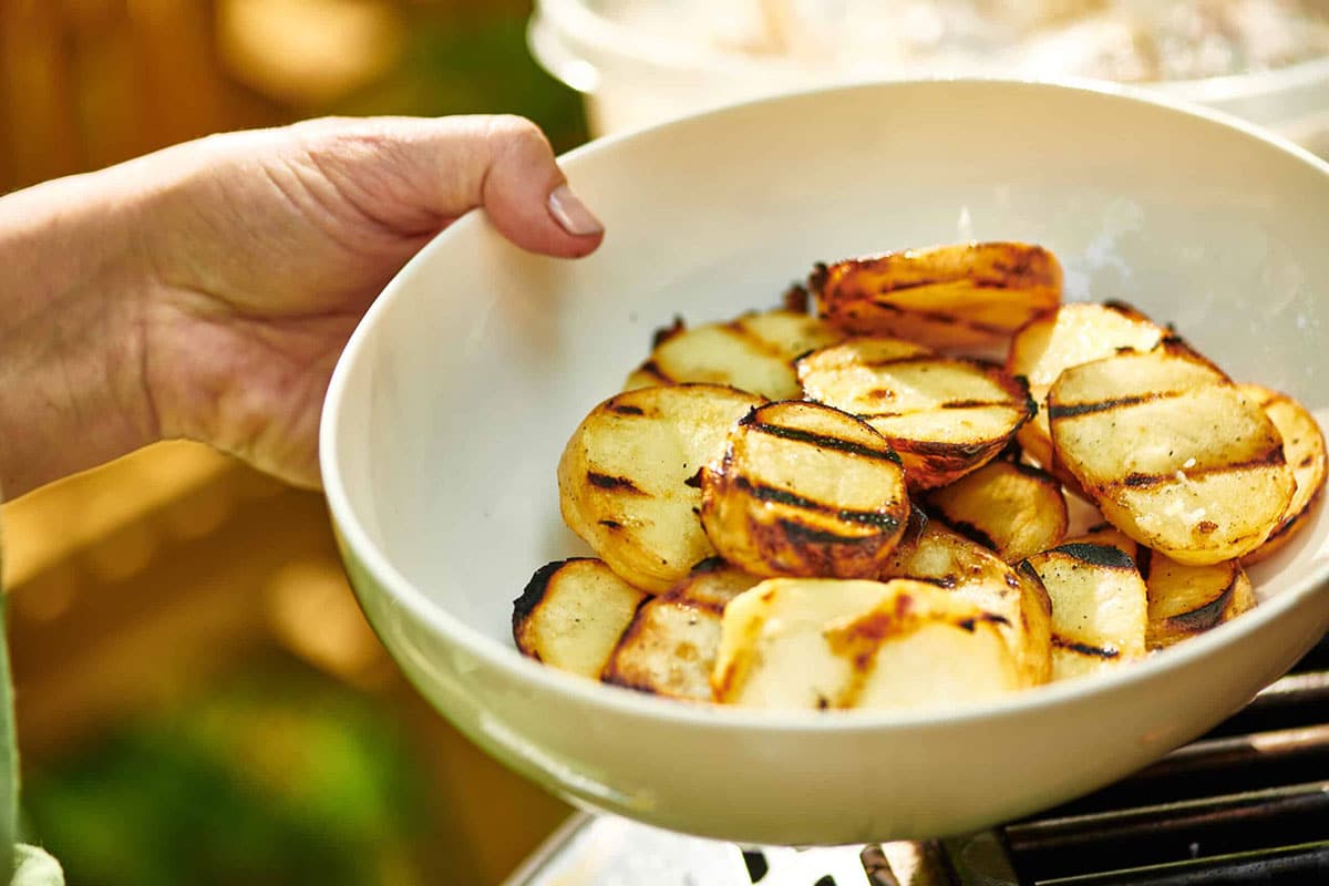 Woman holding bowl of grilled potatoes at BBQ.