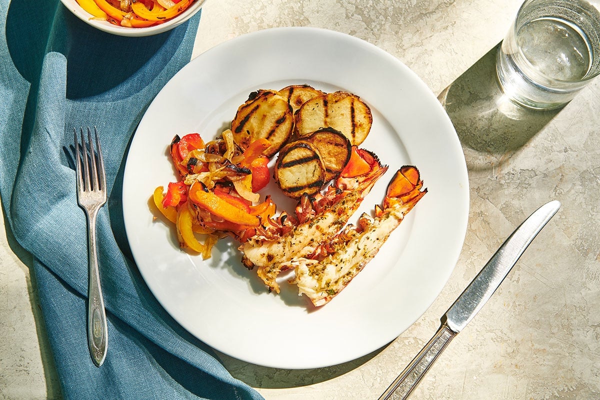 Grilled lobster with grilled peppers and potatoes on plate.