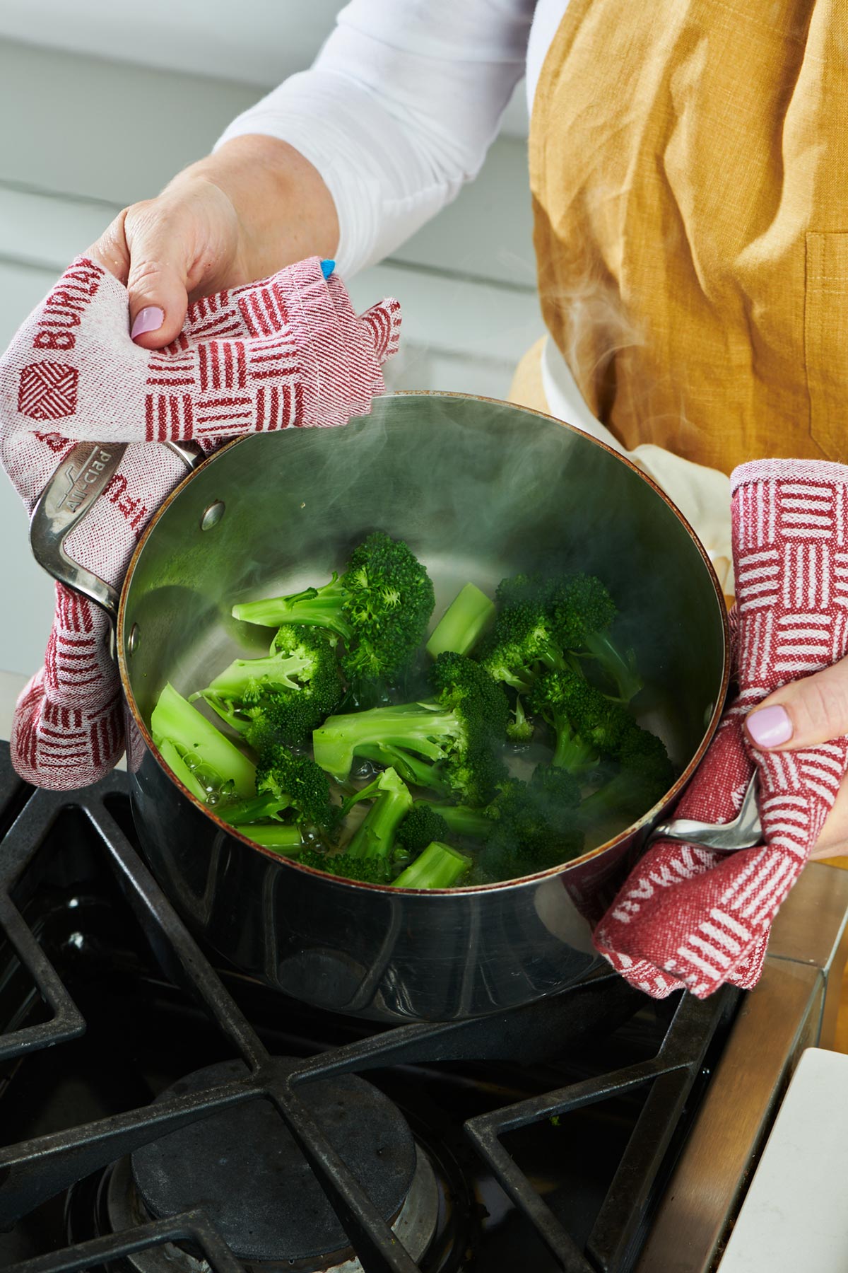 Woman holding pot of steamed broccoli over stove.