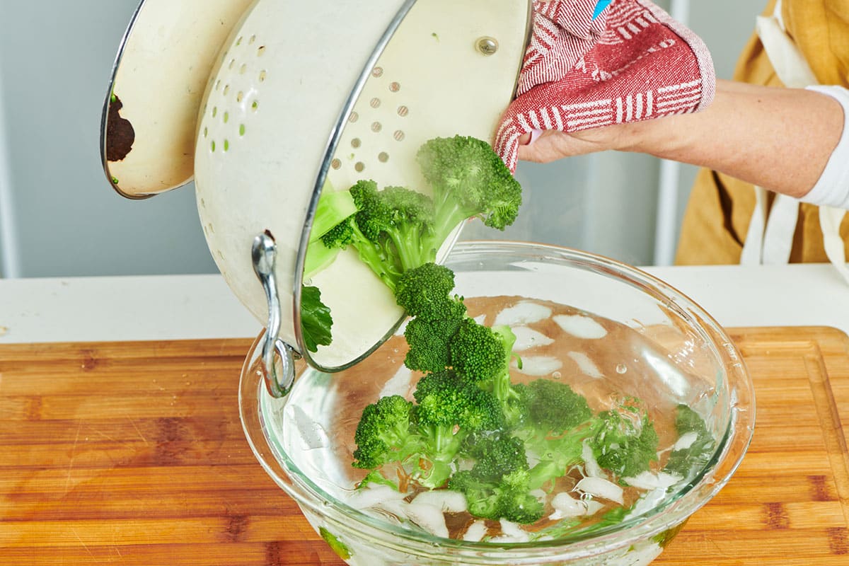 Pouring steamed broccoli into ice water bath.