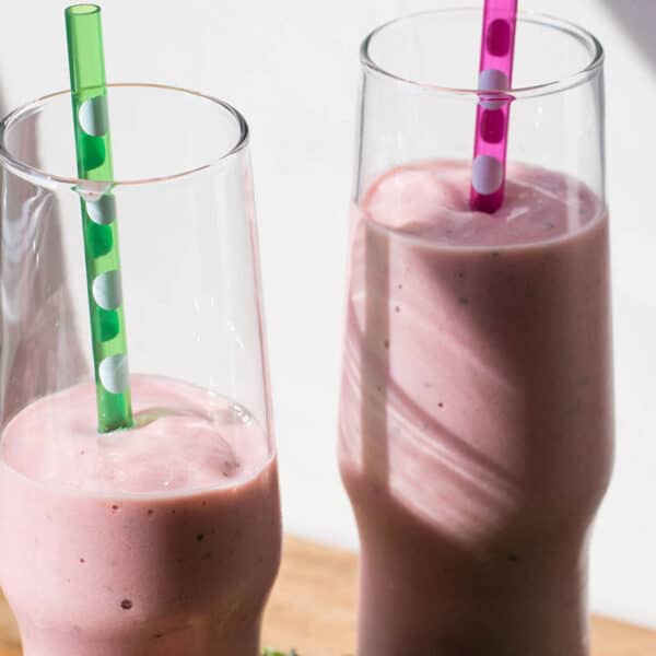 Two ginger, peach, and plum smoothies in glasses with straws.