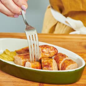 Woman using fork to eat baked Italian sausage.