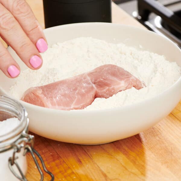 Dredging chicken in bowl of flour.