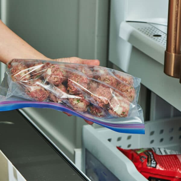 Woman placing freezer bag of meatballs in freezer.