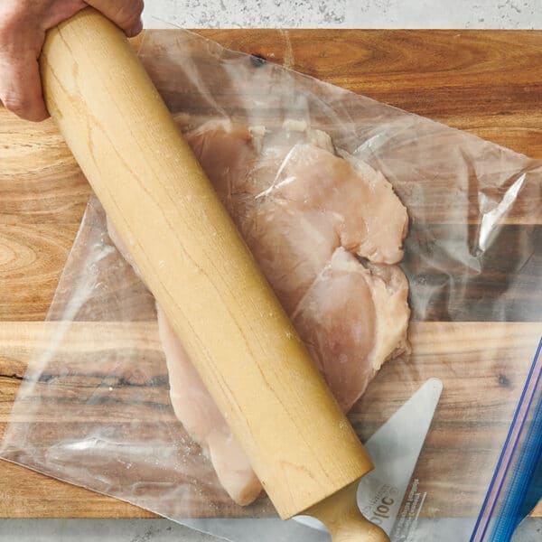 Pounding chicken breast in plastic bag with rolling pin.