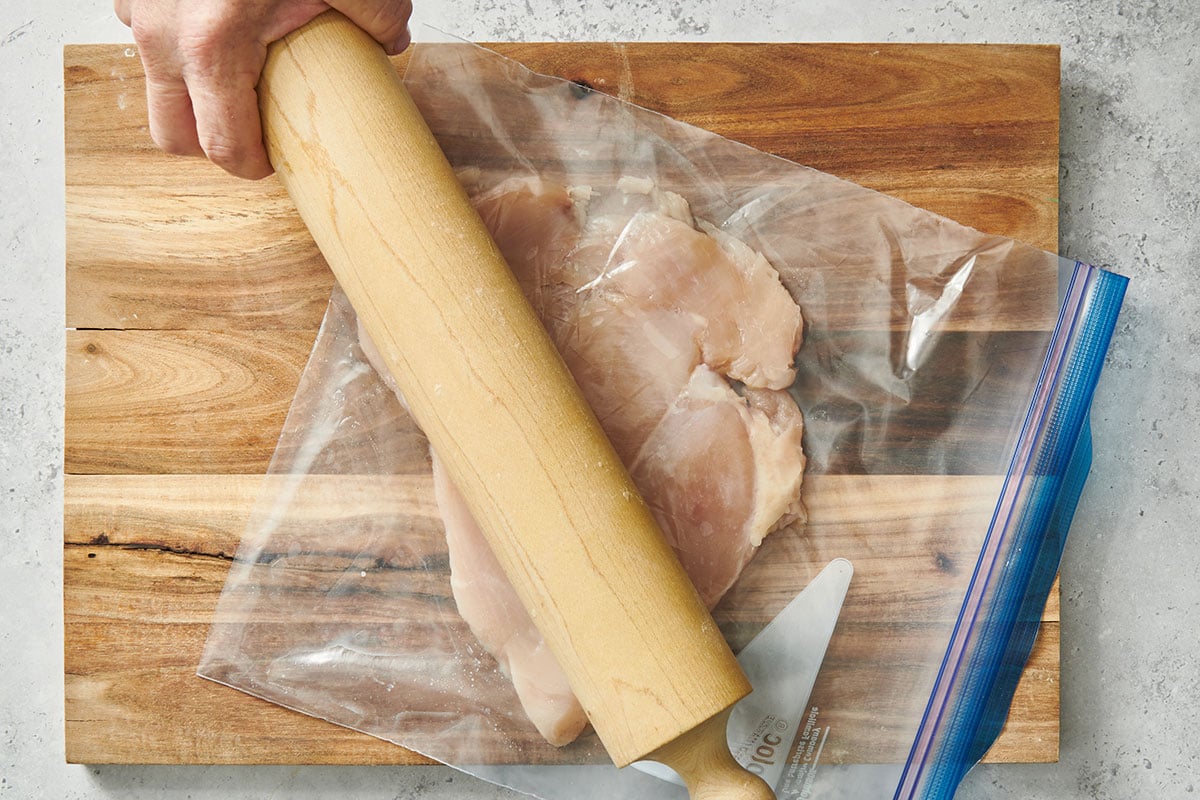 Pounding chicken breast in plastic bag with rolling pin.