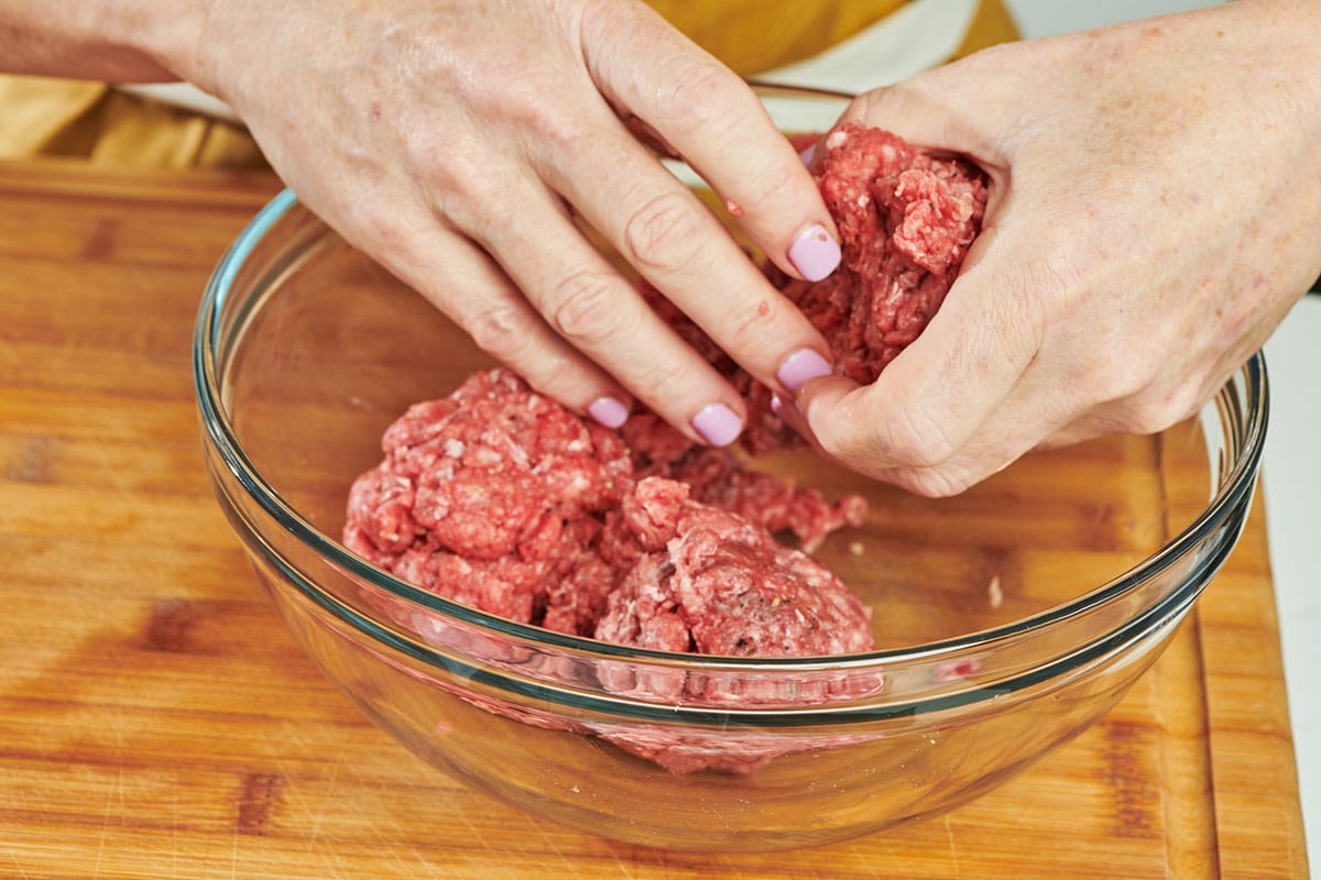 Mixing raw ground beef in bowl.