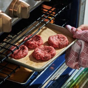 Placing tray of hamburgers in oven.