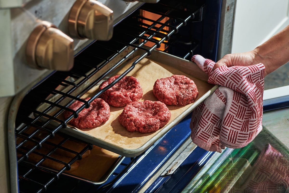 Placing tray of hamburgers in oven.