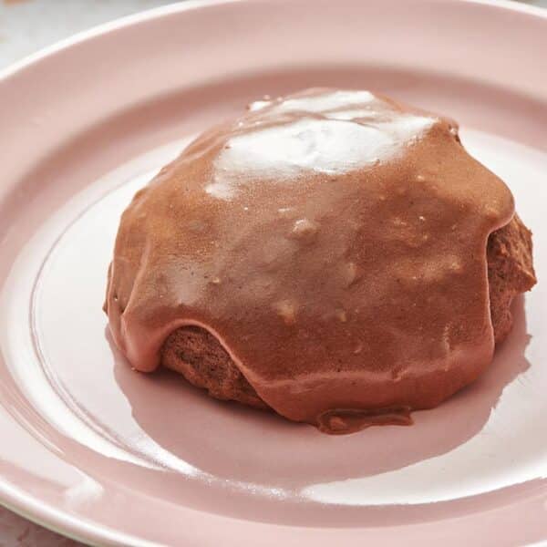 Chocolate pumpkin cookie with chocolate icing on pink plate.