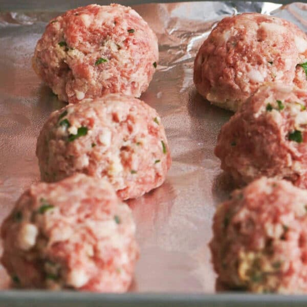 Uncooked meatballs on foil-lined baking sheet.