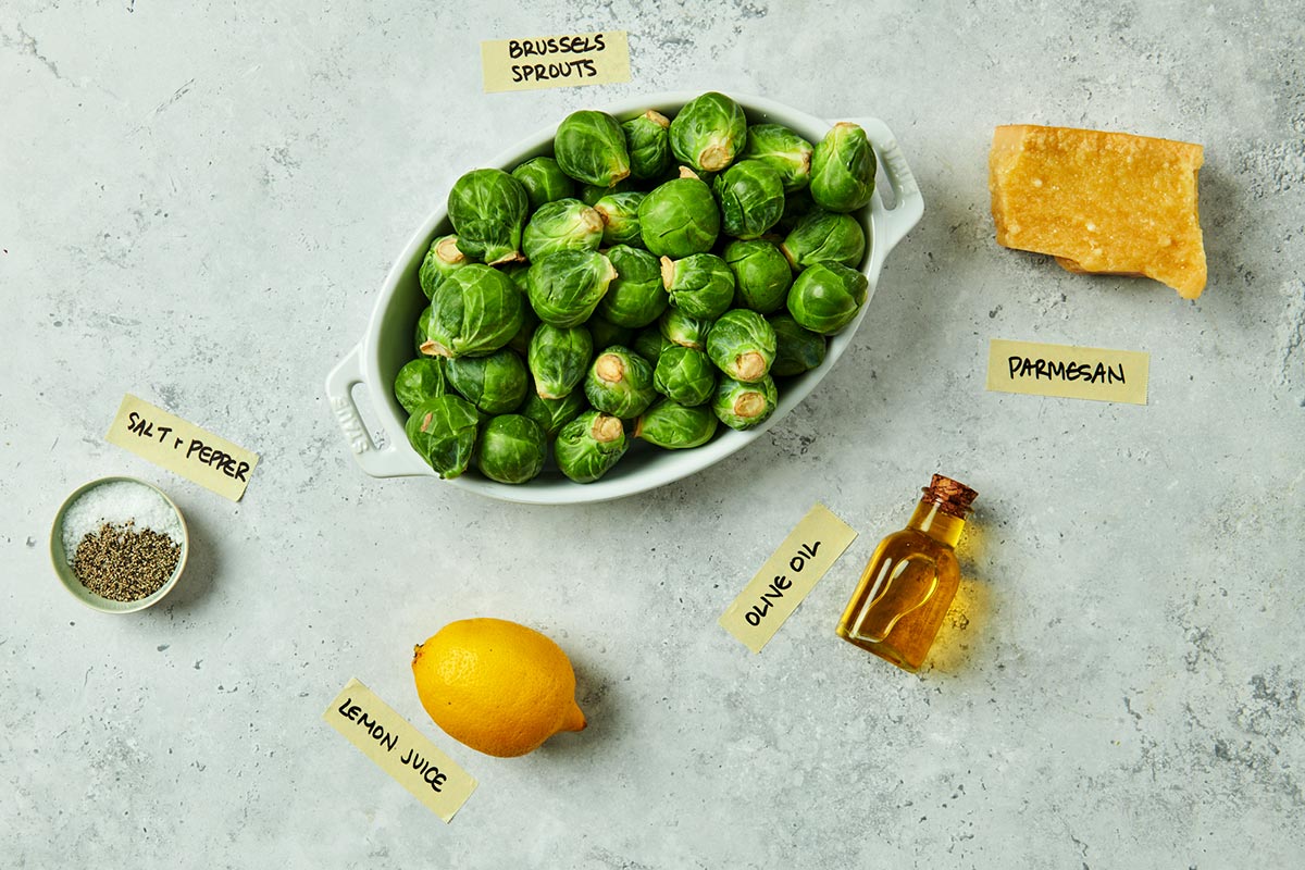 Fresh Brussels sprouts, cheese, and lemon on marble surface.