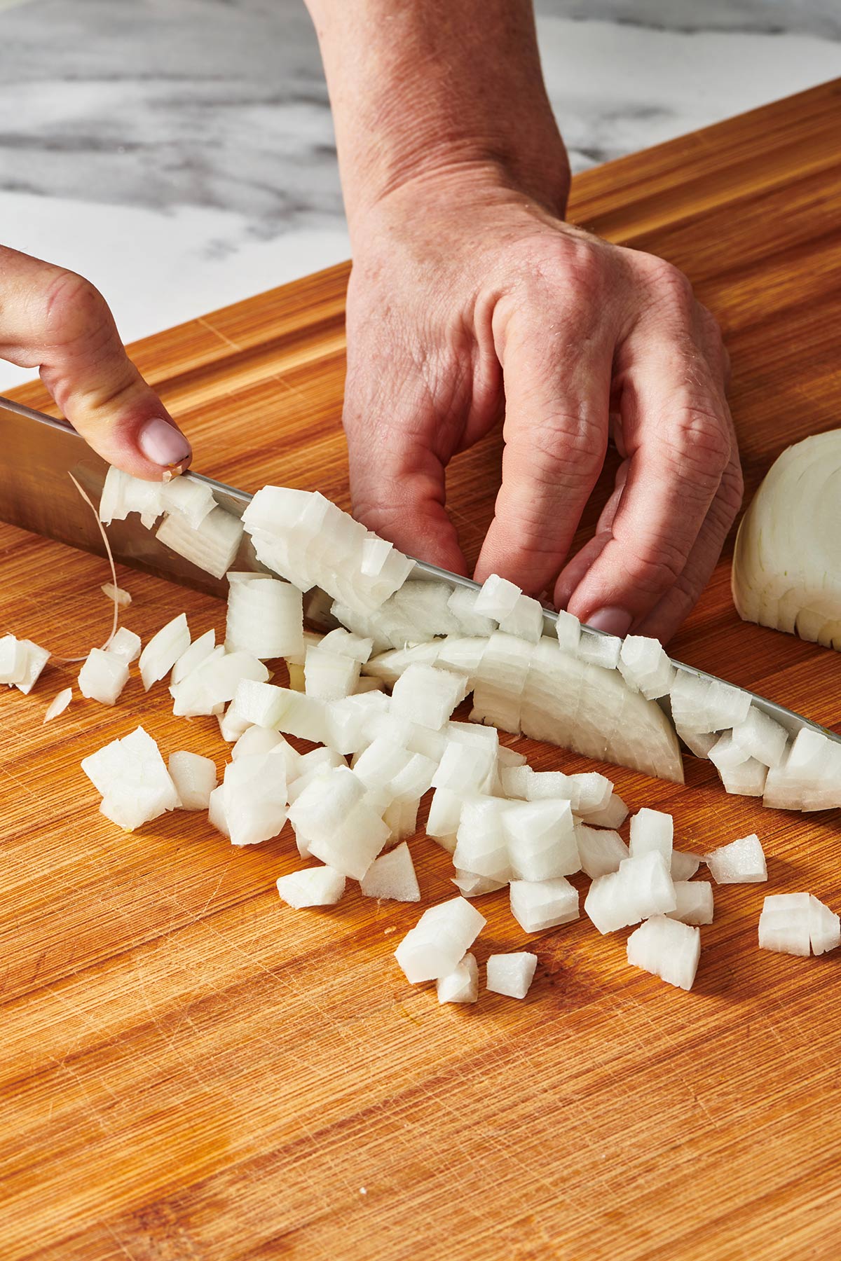 Woman dicing white onion with knife on cutting board.