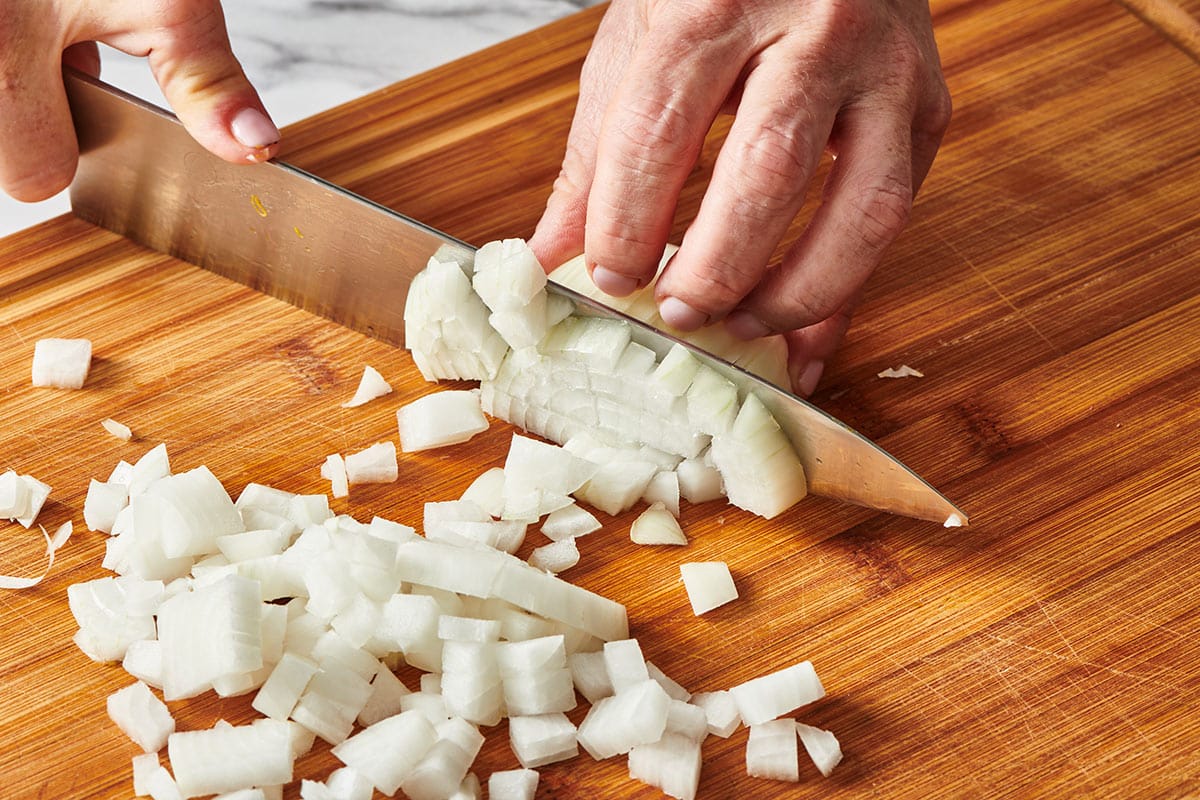 Woman dicing white onion on cutting board.