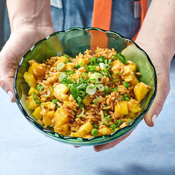 Woman holding green bowl with pineapple fried rice.