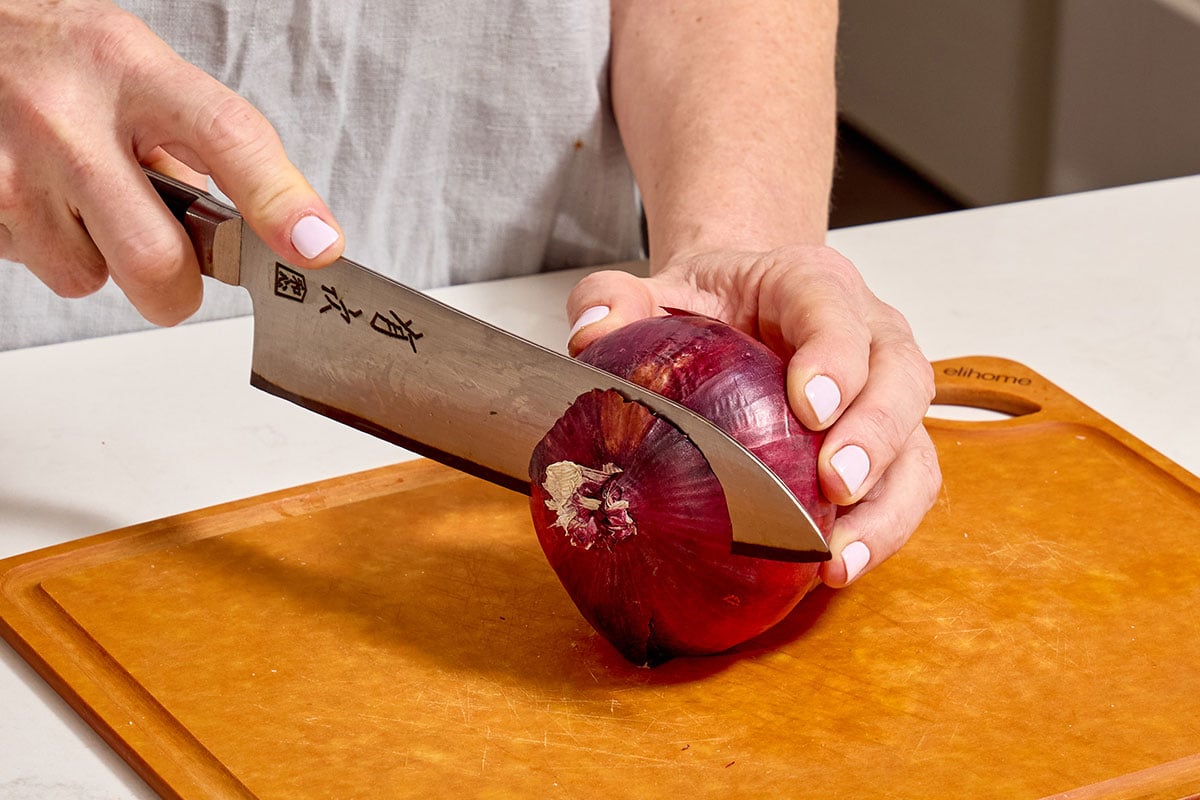 Slicing stem off red onion with knife.