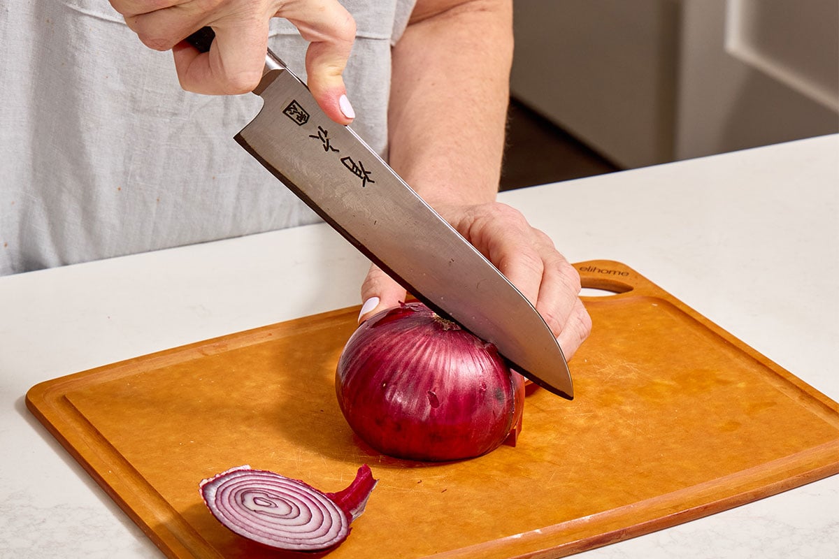 Cutting white onion in half with knife.