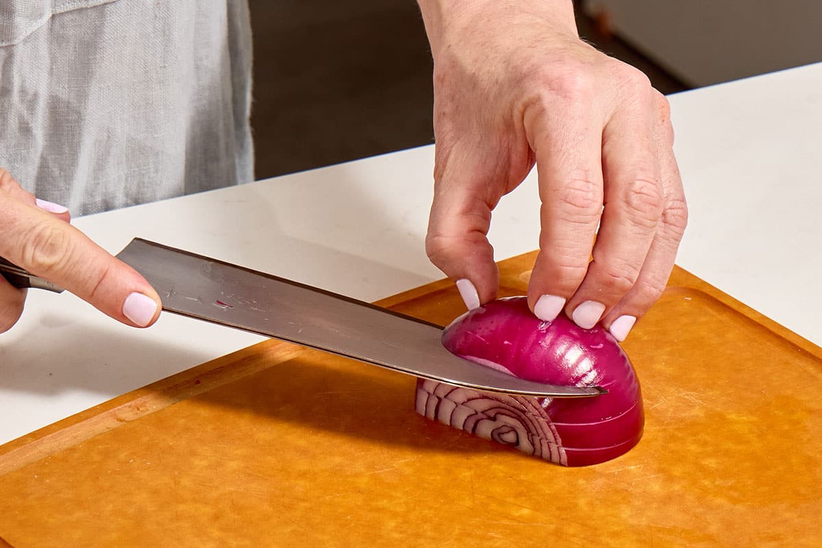 Woman cutting red onion slices with knife.