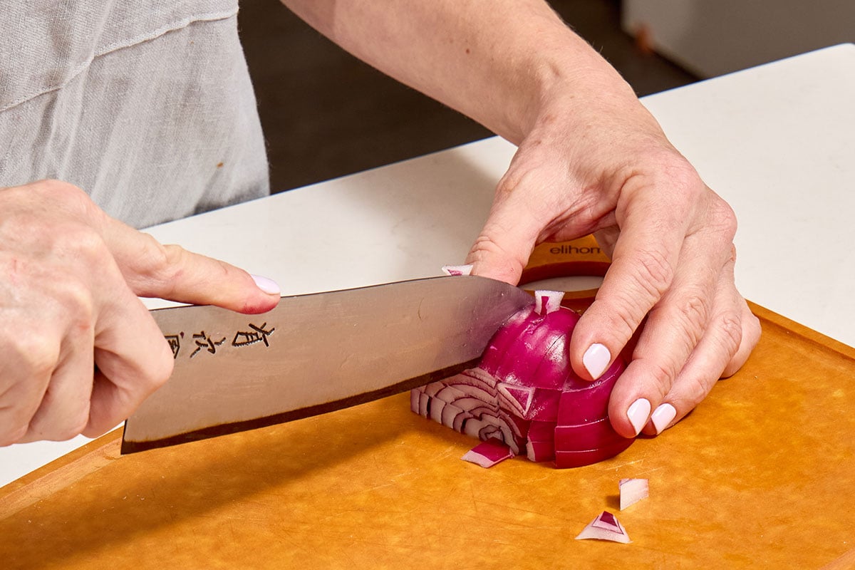 Woman slicing red onion into strips.