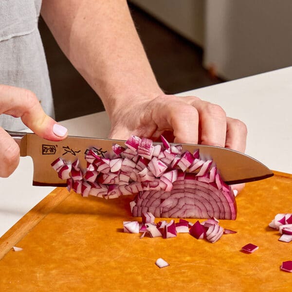 Woman dicing red onion on cutting board with knife.