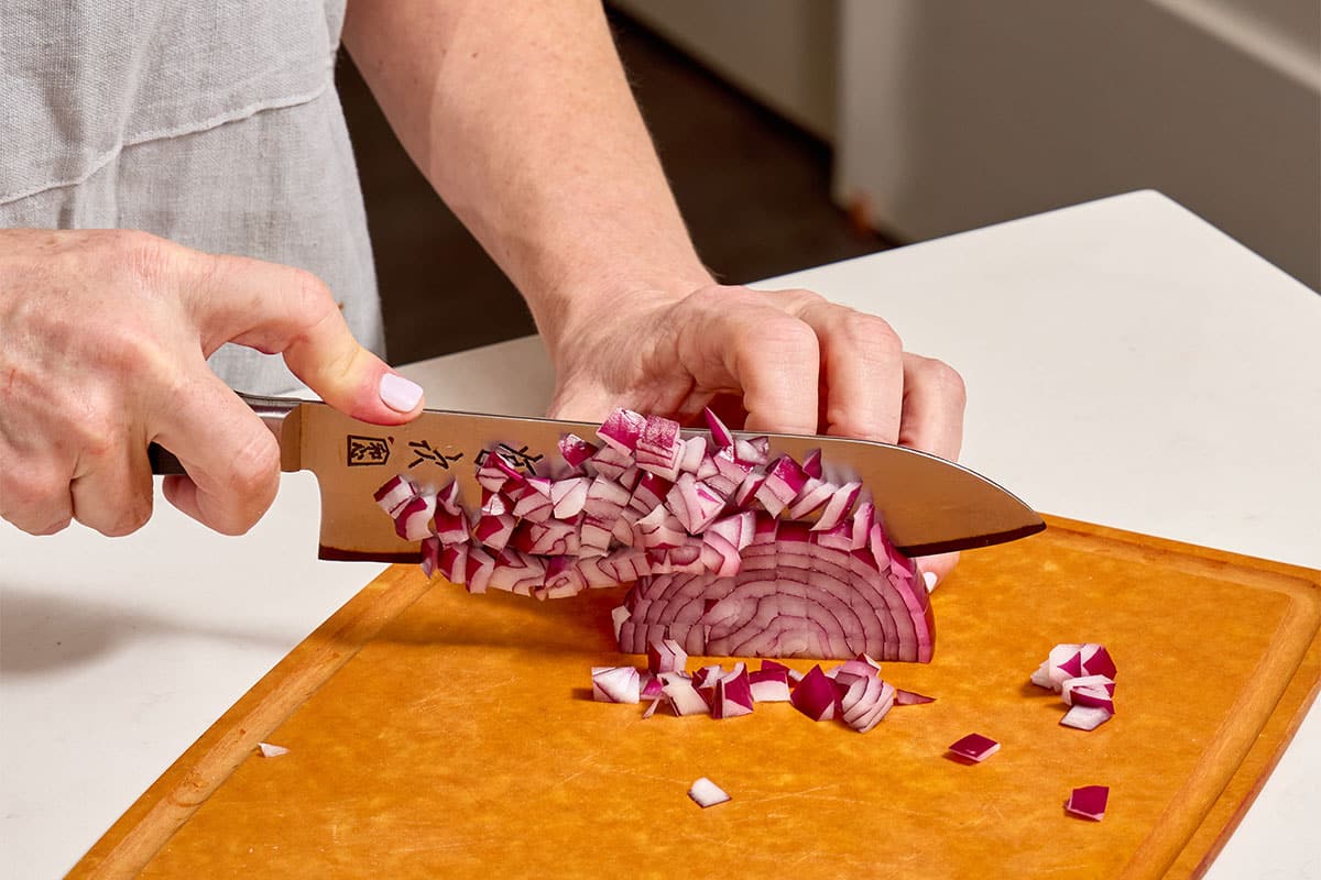 Woman dicing red onion on cutting board with knife.