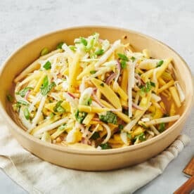 Vietnamese green mango salad in brown bowl on table.