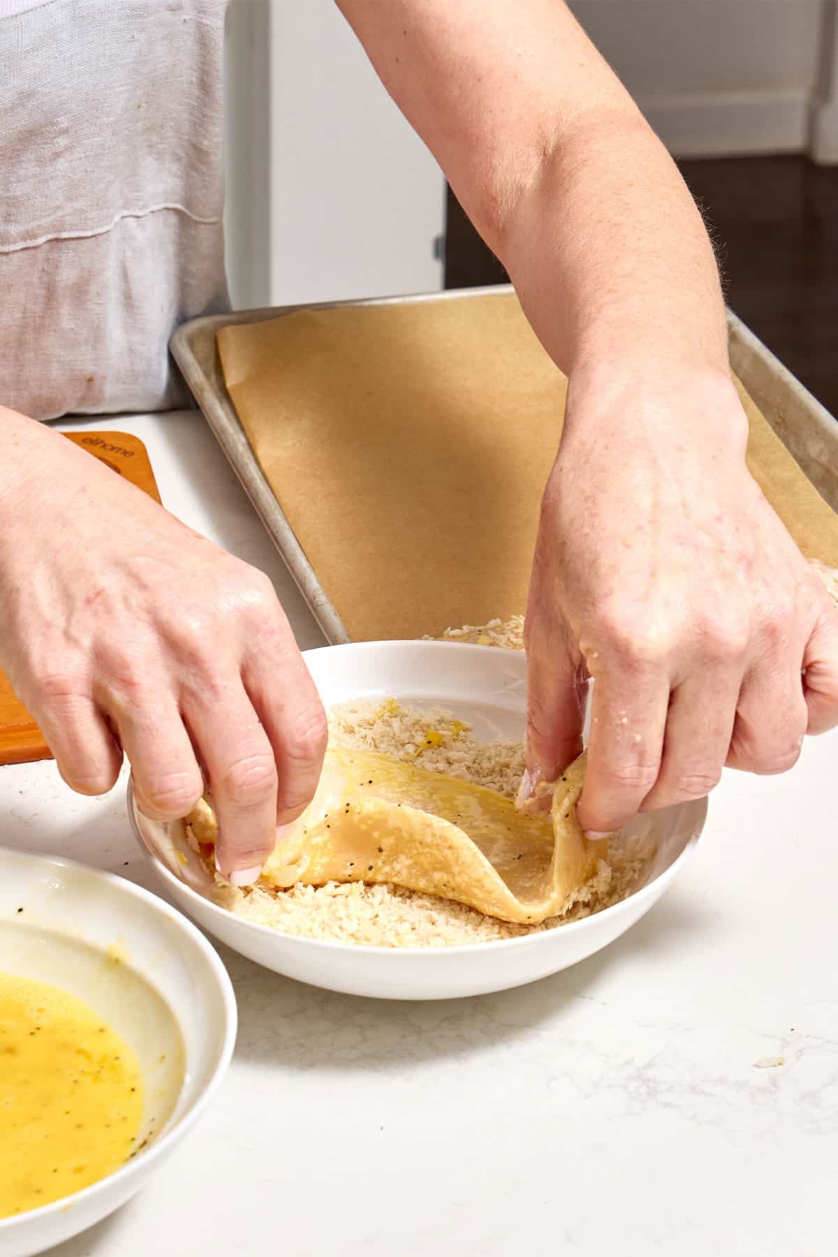 Woman dredging egg-coated chicken cutlet in panko breadcrumbs.