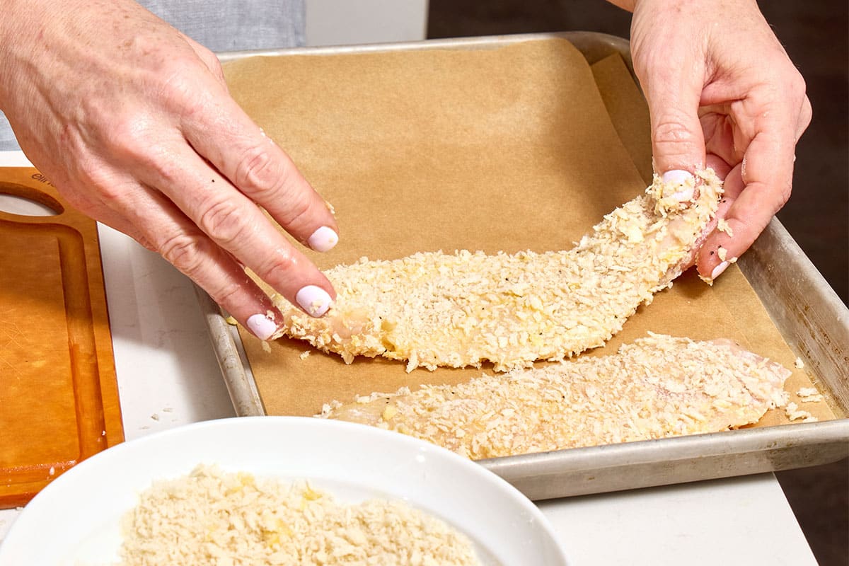 Woman placing breaded chicken cutlet on parchment-lined baking sheet.