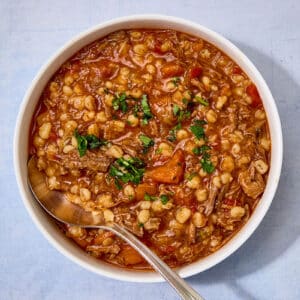 Brisket and barley soup in white bowl with spoon.