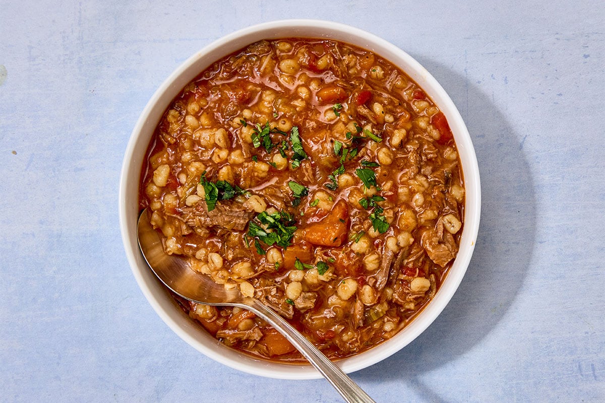 Brisket and barley soup in white bowl with spoon.