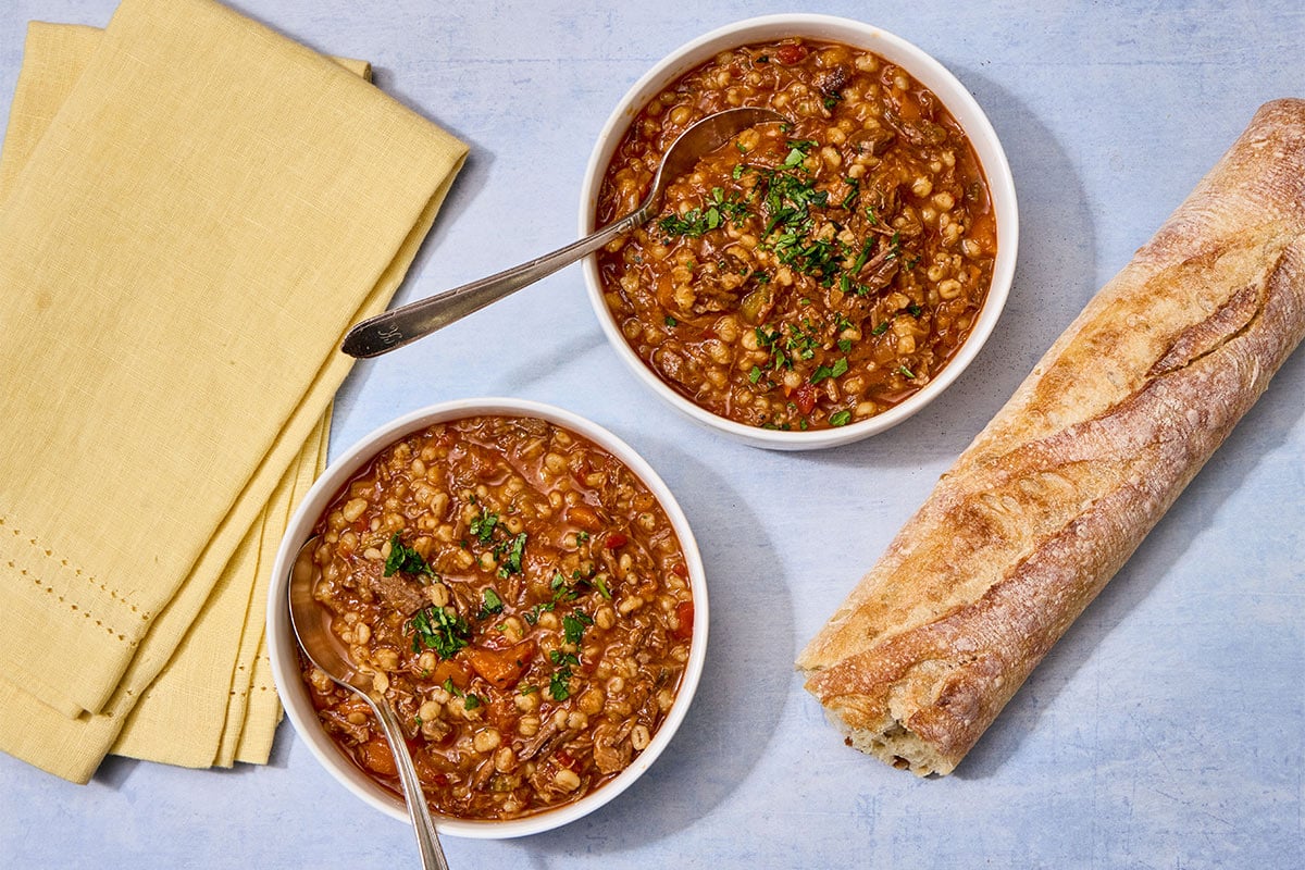 Brisket barley soup in bowls on table with bread.