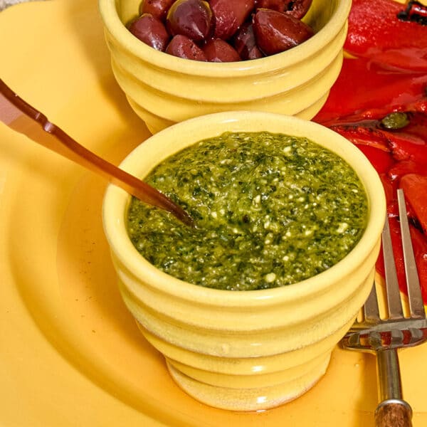 Pumpkin seed pesto in yellow bowl with spoon on platter.