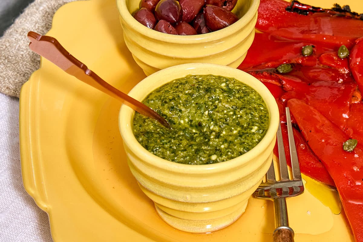 Pumpkin seed pesto in yellow bowl with spoon on platter.