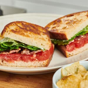 BLT sandwich cut in half on white plate with chips.