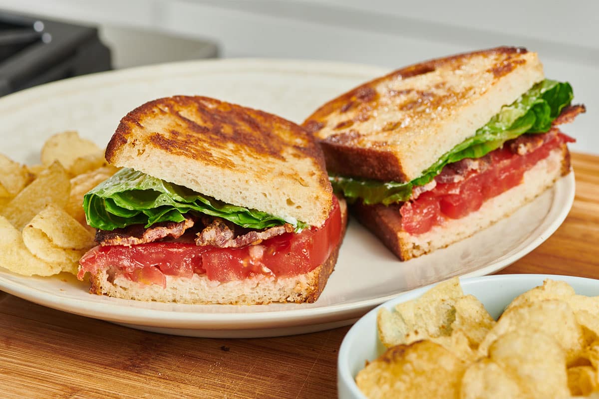 BLT sandwich cut in half on white plate with chips.