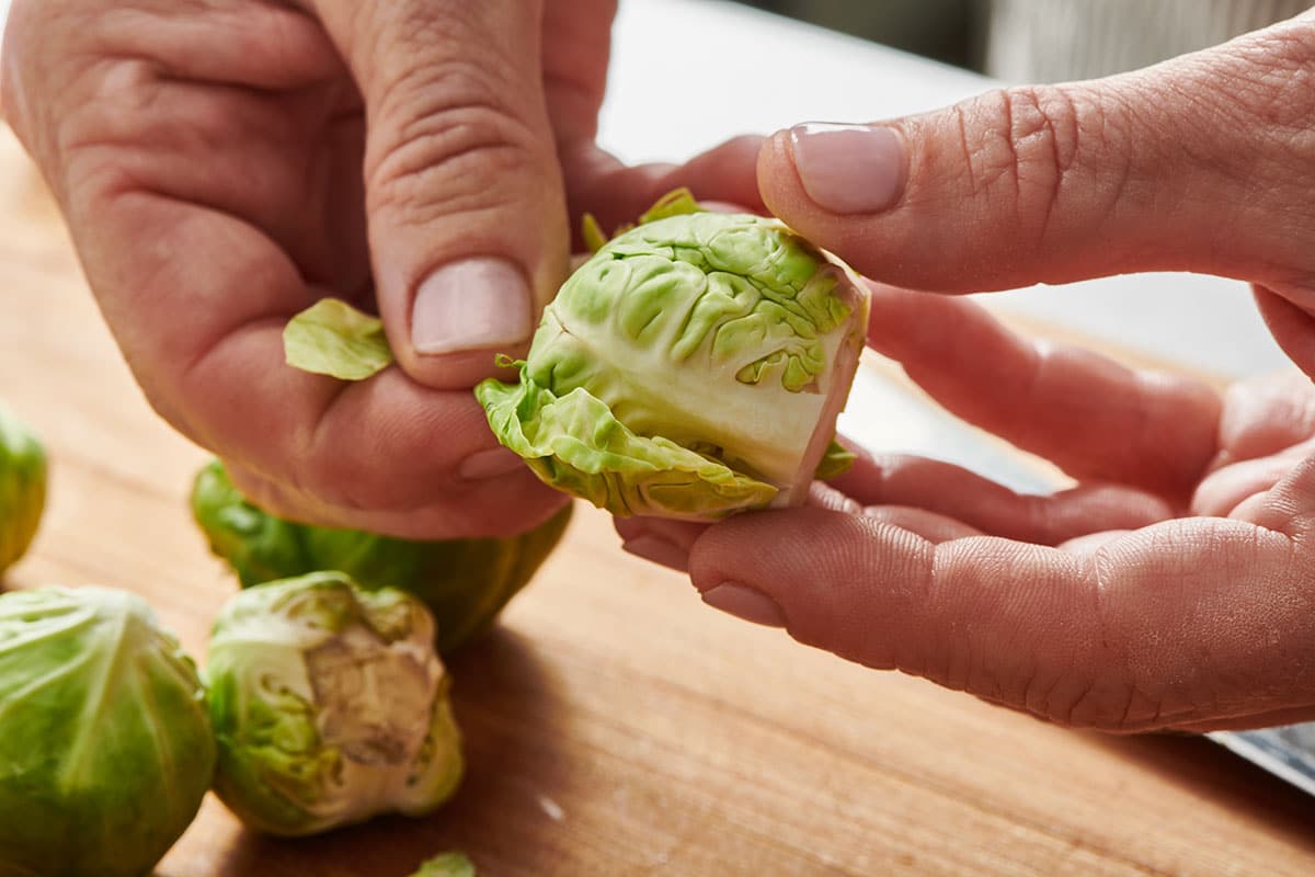 Woman removing out leaves from fresh Brussels sprouts.