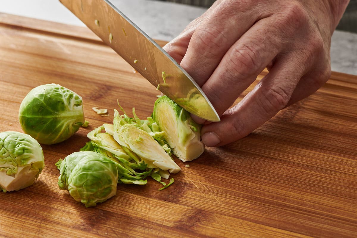 Slicing Brussels sprout into thin shreds with knife.