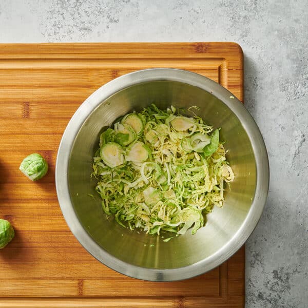 Shredded and whole Brussels sprouts in bowl and on cutting board.