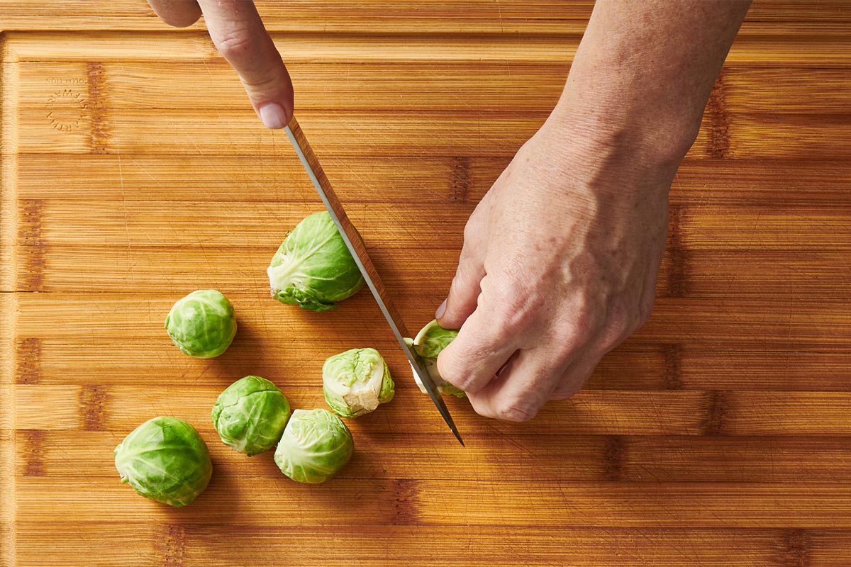Woman cutting ends off fresh Brussels sprouts with knife.