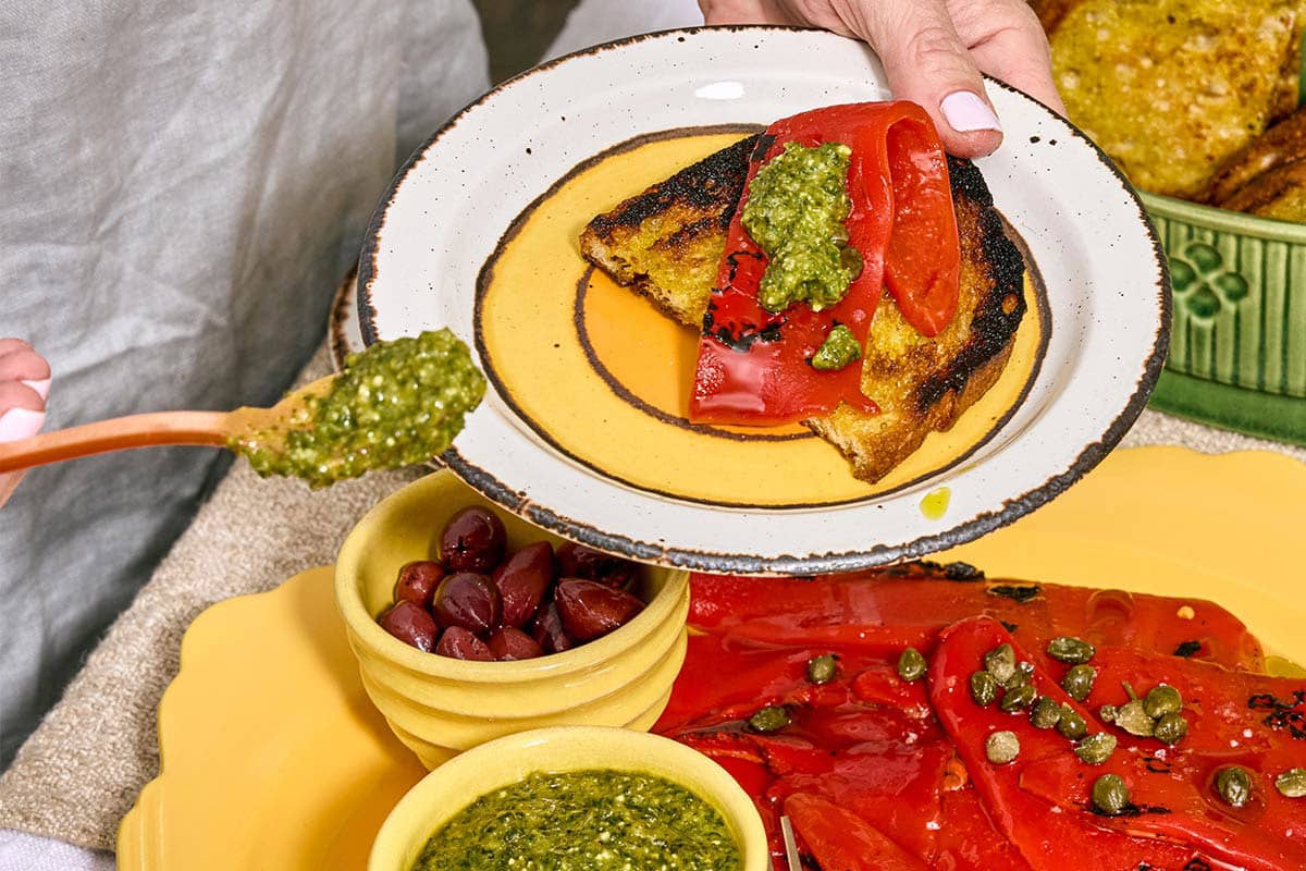 Woman topping pepita pesto on roasted peppers withe spoon.