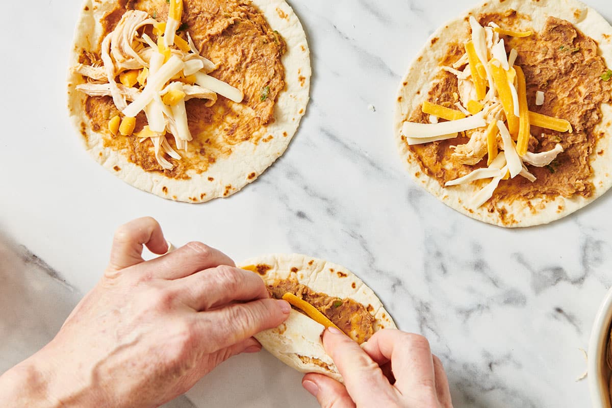 Woman rolling tortillas with flauta fillings.