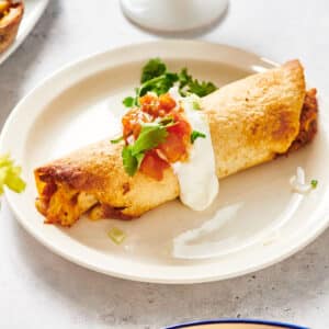 Chicken flauta on plate with sour cream, salsa, and cilantro.