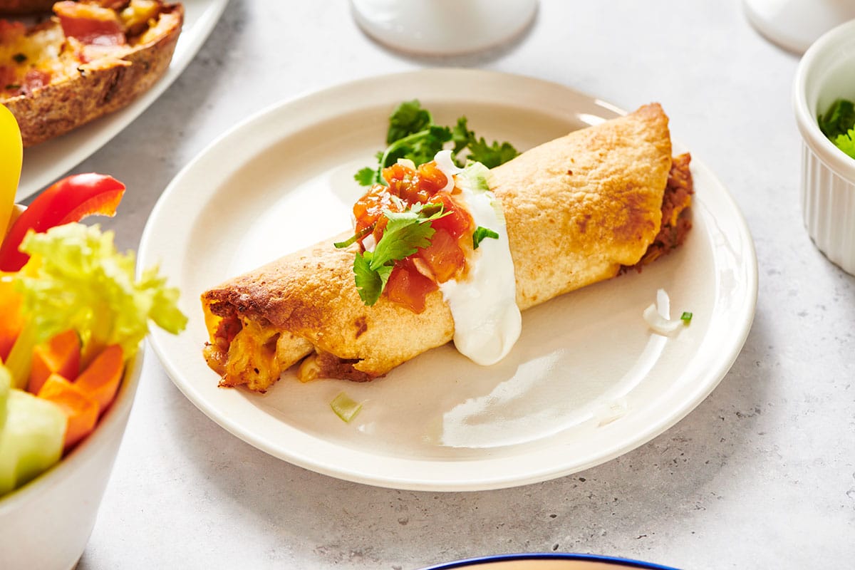 Chicken flauta on plate with sour cream, salsa, and cilantro.