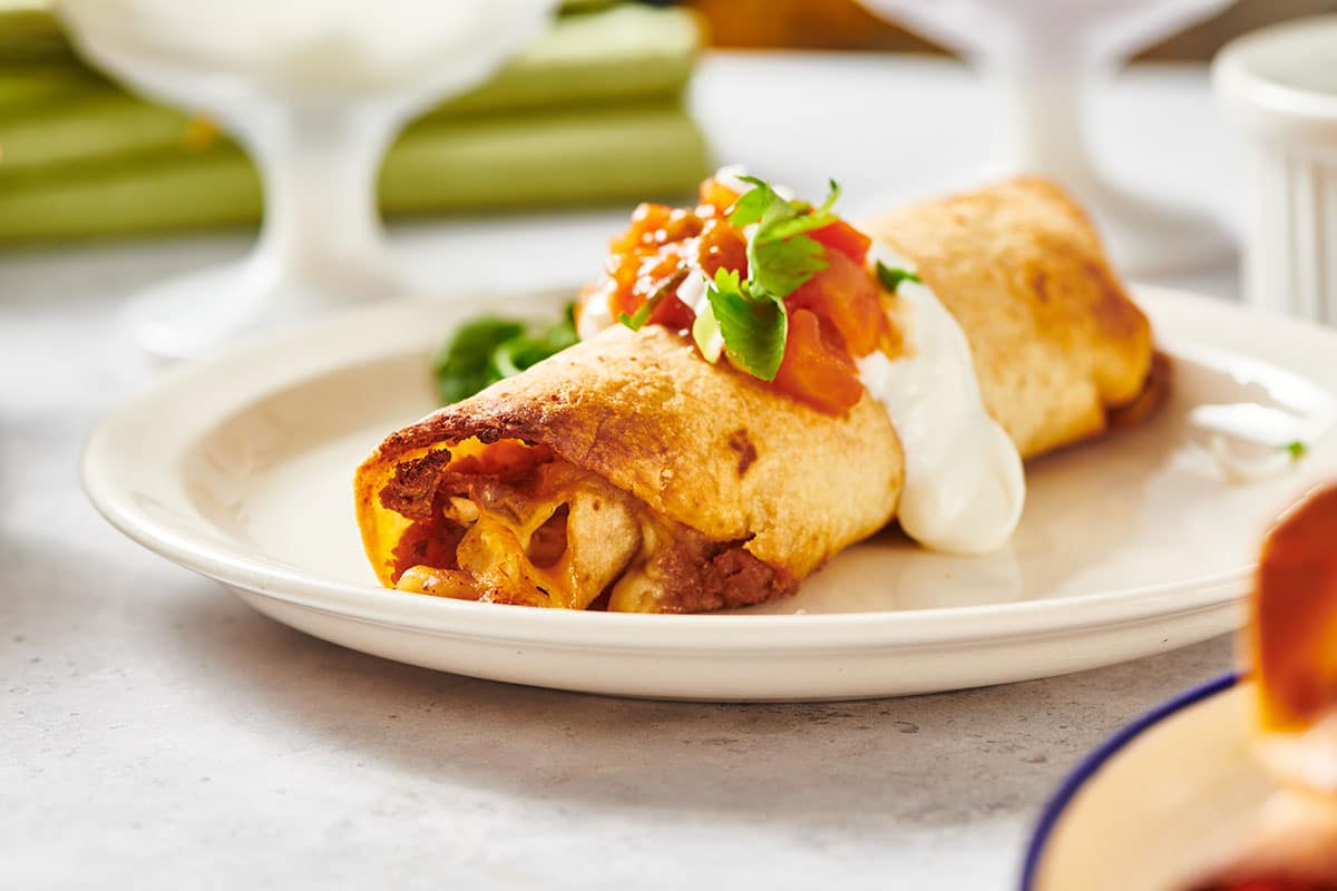 Chicken flauta on white plate with toppings.
