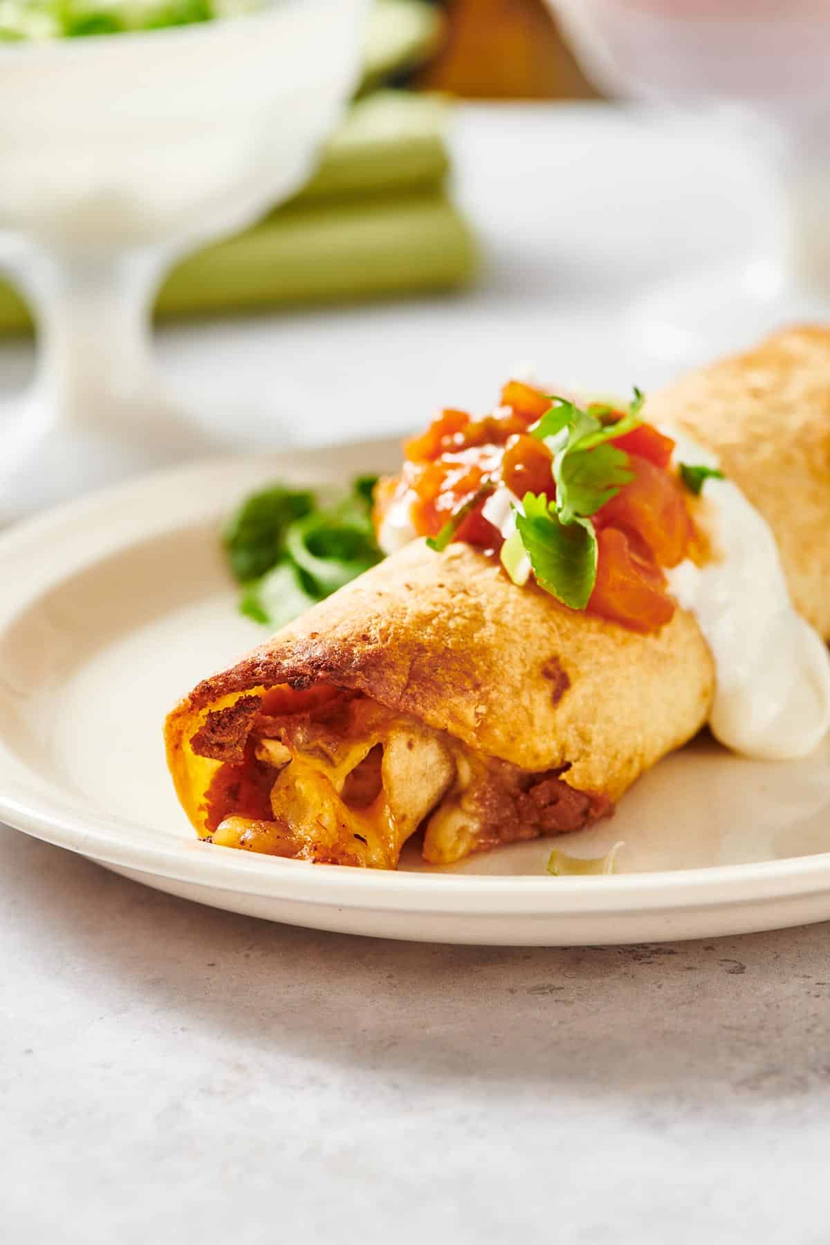 Baked chicken flauta on white plate with toppings.