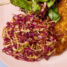 Chili crunch cole slaw on pink plate with chicken and salad.