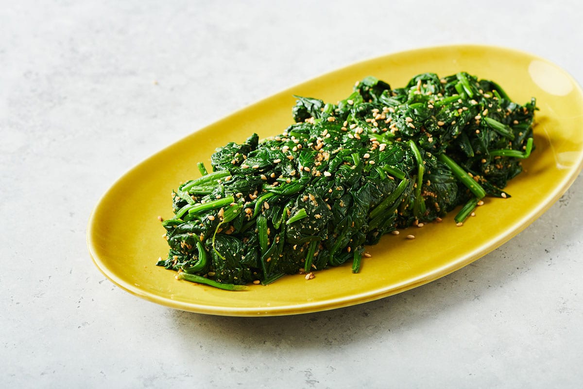 Japanese spinach gomaae with toasted sesame seeds and bonita flakes on yellow platter.